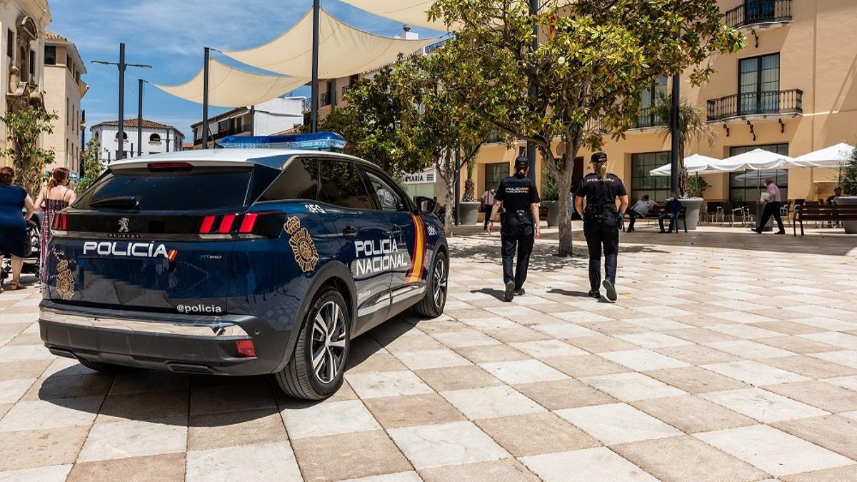 Imagen de archivo de un coche de la Policía Nacional y dos agentes patrullan en una calle