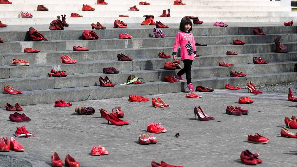 Una niña pasa por una composición de zapatos rojos de mujer en una escalera.