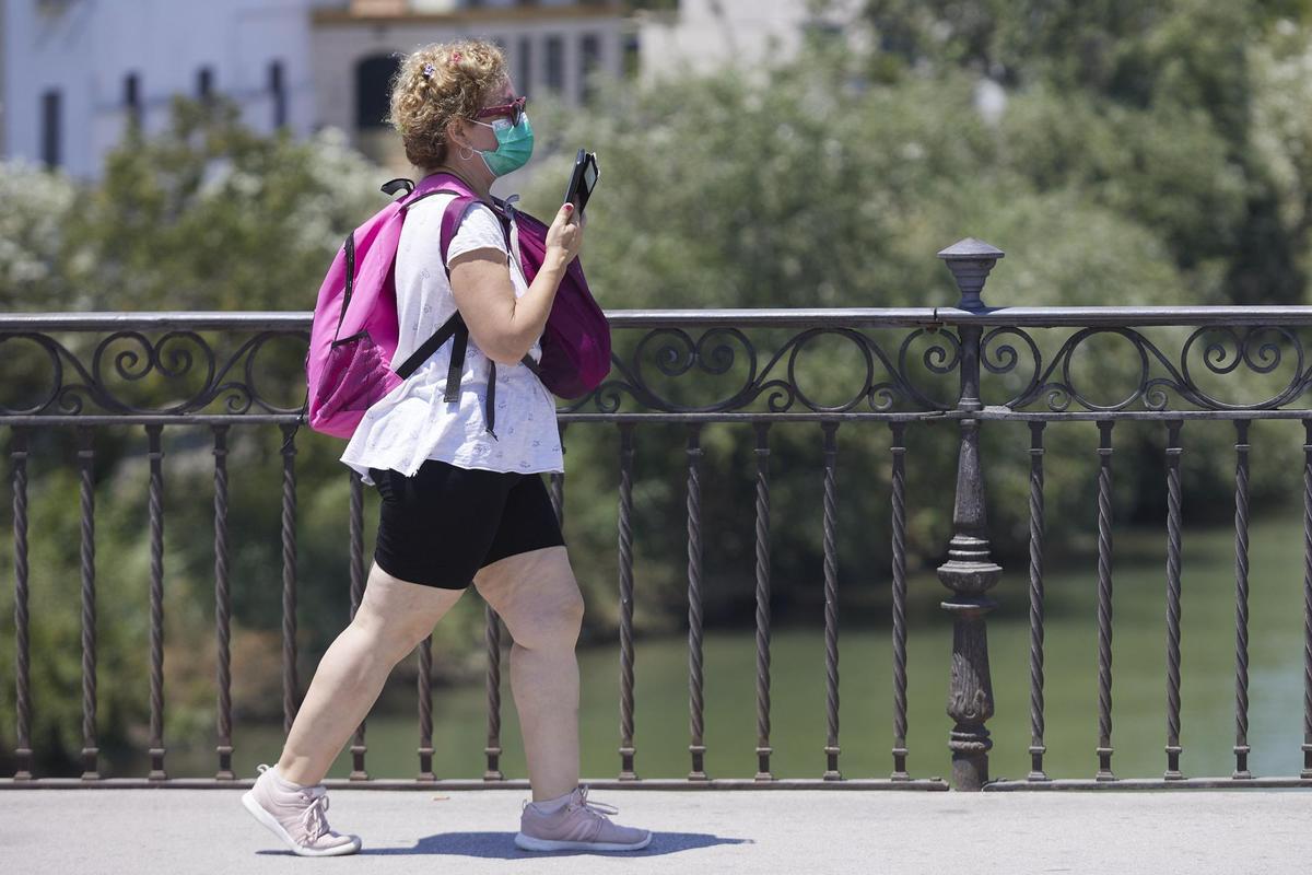 Una señora, que porta mascarilla, cruza el puente de Isabel II en el primer día de la segunda ola de calor, a 7 de julio de 2022 en Sevilla (Andalucía, España)