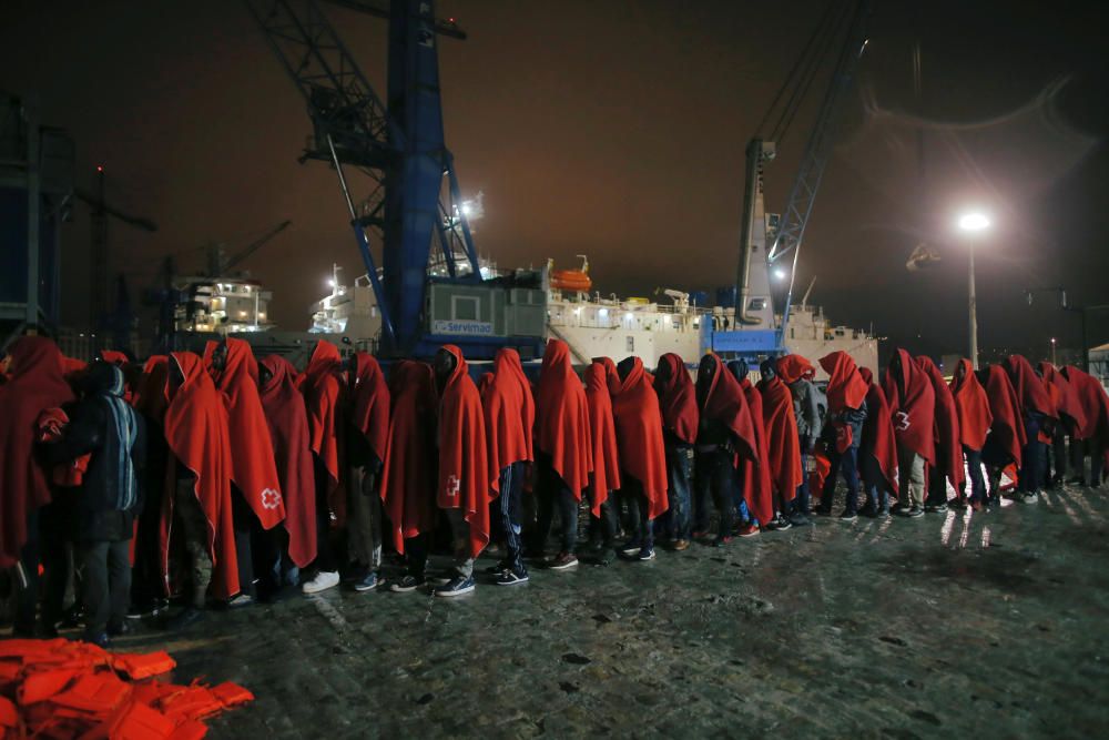 Migrants stand under the rain after disembarking ...