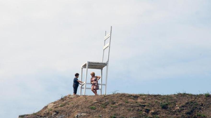 Dos vecinas conversan  apoyadas en la misteriosa silla que apareció en el monte de Meira.  // G. Núñez