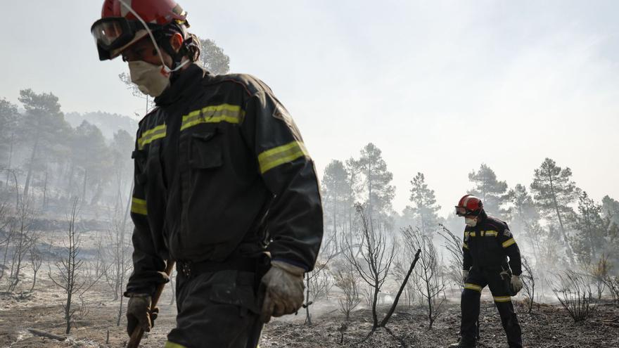 Dos bomberos forestales repasan la zona quemada tras el paso de las llamas en una zona próxima a Montán. | BIEL ALIÑO/EFE