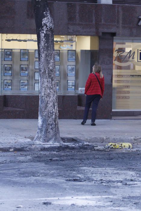 Carrers amb restes de mobiliari urbà cremat, contenidors per terra i treballadors de la brigada treballant