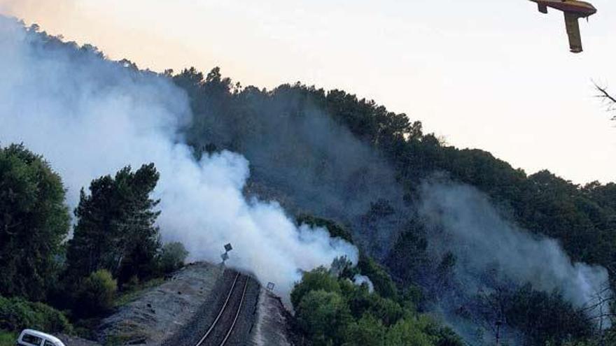 Un hidroavión sobrevuela un foco del incendio que irrumpe en la vía del tren, entre las estaciones de Maside y Santa Cruz de Arrabaldo.  // Brais Lorenzo