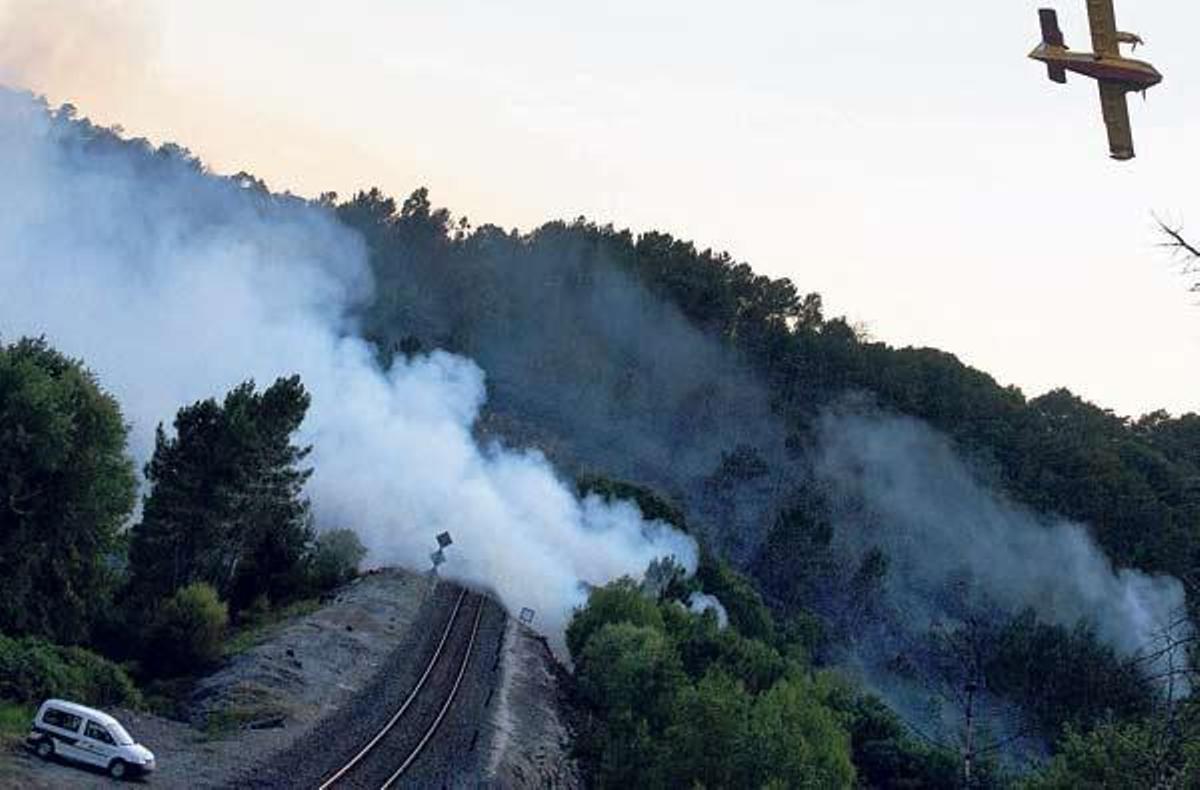 Un hidroavión sobrevuela un foco del incendio que irrumpe en la vía del tren, entre las estaciones de Maside y Santa Cruz de Arrabaldo.  // Brais Lorenzo