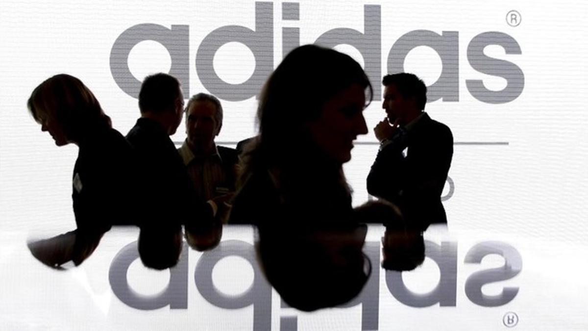 Silueta de los accionistas de Adidas delante del logo de la marca