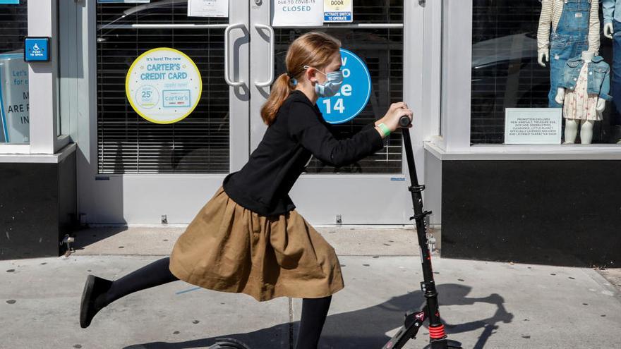 Una joven judía ultraortodoxa pasa en patinete por una tienda cerrada en Nueva York.