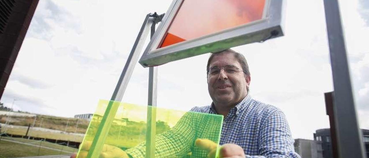 Amador Menéndez muestra uno de los vidrios tintados que generan electricidad junto al prototipo de ventana que tiene instalada esa tecnología.