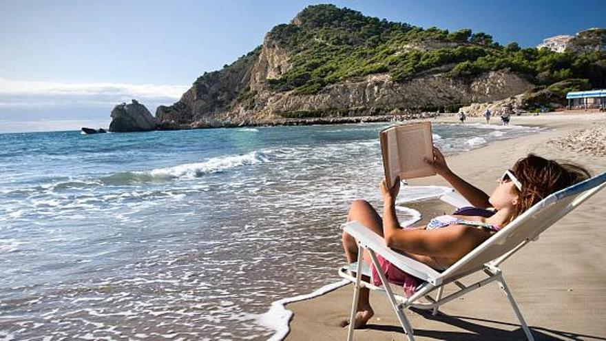 Una joven lee un libro en la orilla de la playa, en una imagen tomada en la cala de Finestrat.