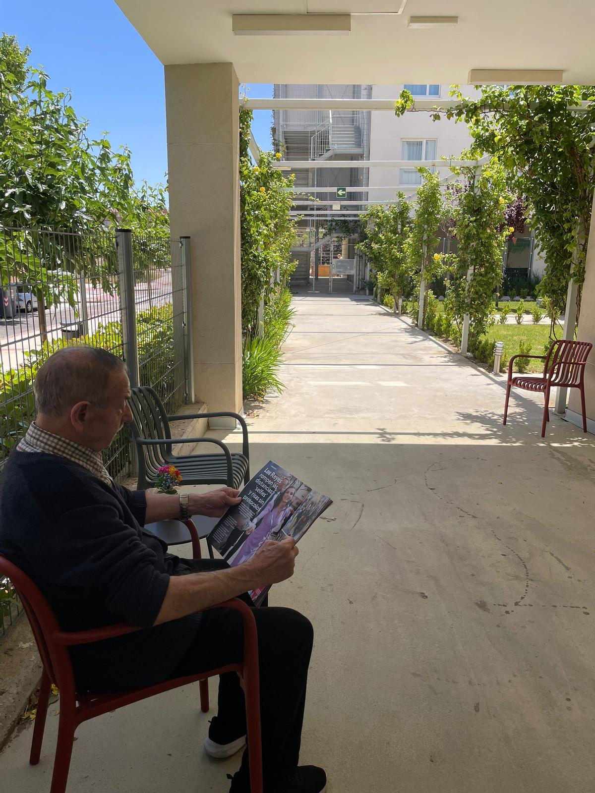 Un residente del centro Rey Ardid Rosales de Zaragoza leyendo una revista en la sombra.