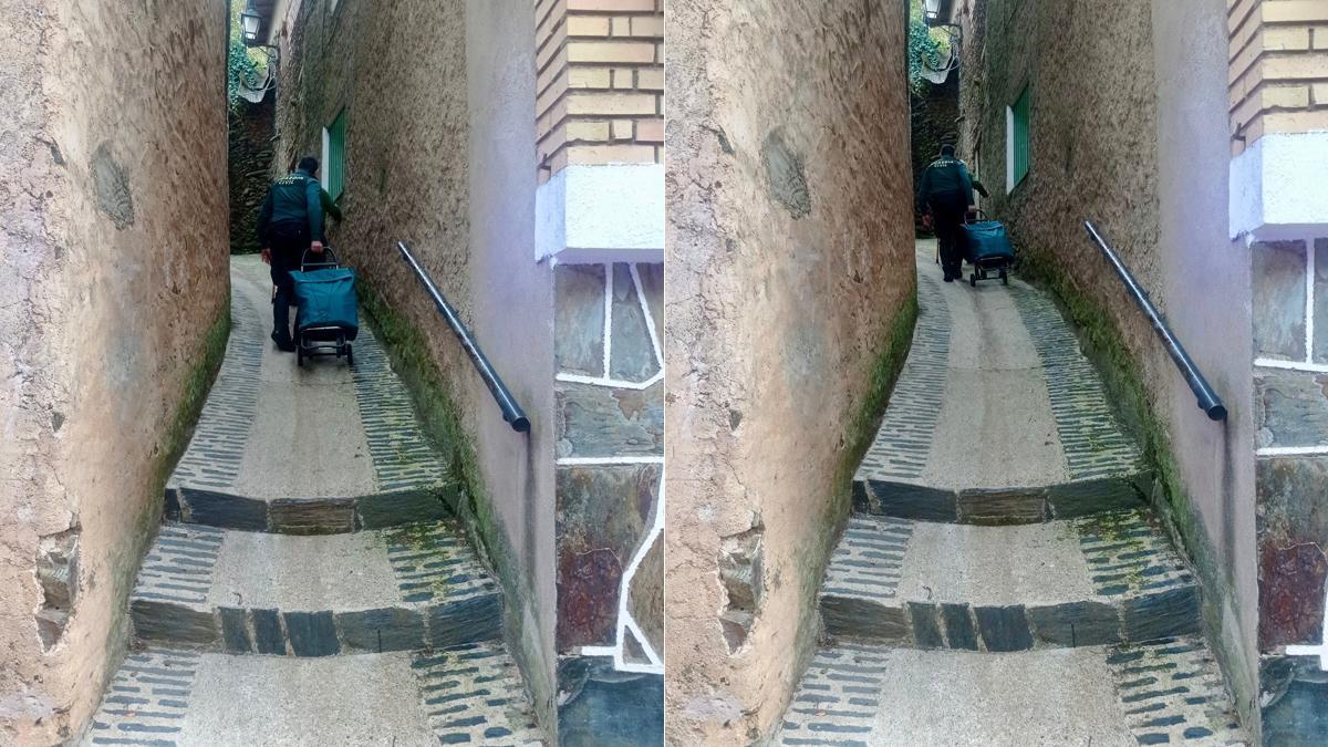 Un guardia civil ayuda a una mujer mayor a llevar el carrito de la compra en Robledillo de Gata.