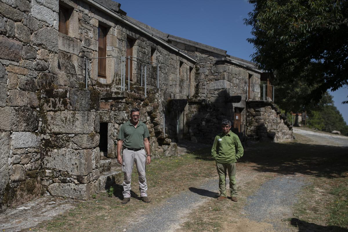 Los dos operarios que se ocupan del mantenimiento de la aldea, ante una de las viviendas restauradas. // BRAIS LORENZO