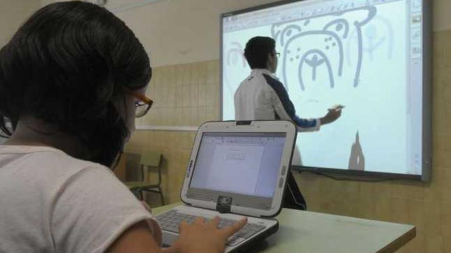 Una alumna trabaja en su ordenador y otro estudiante en la pizarra digital de su clase. / víctor echave