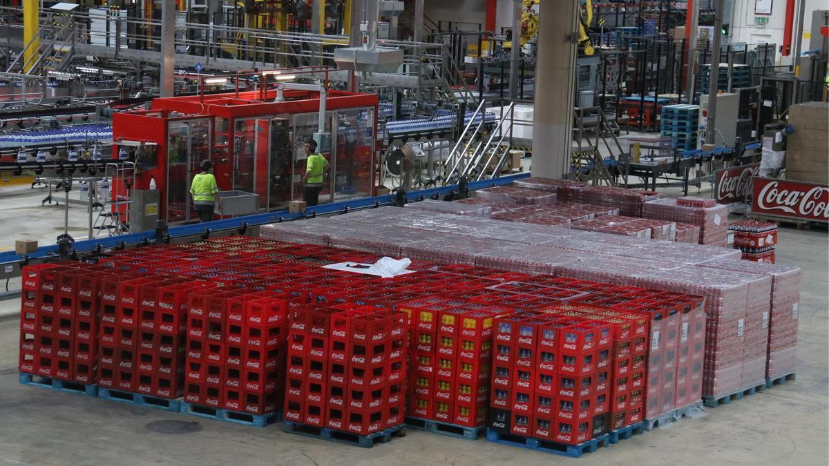 Dos operaris treballant a la fàbrica de Coca-Cola de Martorelles davant de milers d'ampolles col·locades en caixes