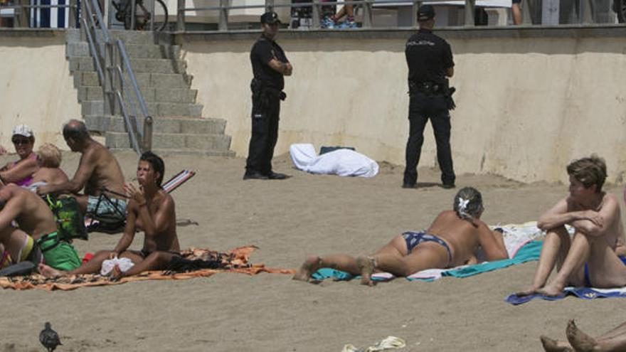 Dos agentes de la Policía Nacional custodian el cadáver en Las Canteras mientras los bañistas toman el sol, ayer.