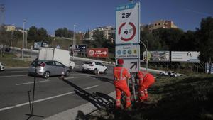 Unos operarios colocan una de las señales que restringe la circulación a los vehículos más contaminantes en L’Hospitalet de Llobregat, esta mañana