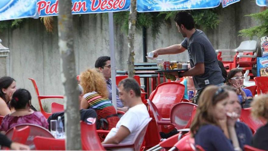 Un camarero sirve a varios clientes en la terraza de un bar.