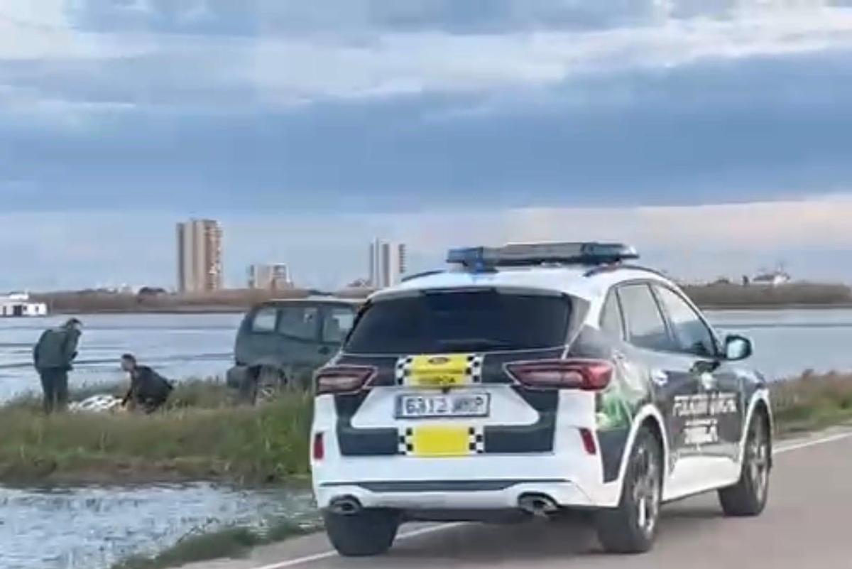 Un vehículo de la Policía Local de Sueca en el lugar en el que se produjo el accidente, con el herido a la izquierda.