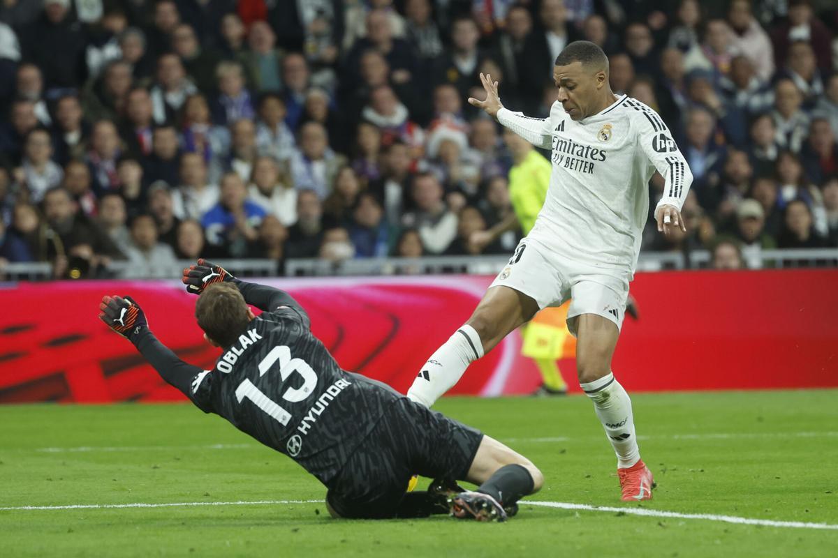 MADRID, 08/02/2025.- El delantero del Real Madrid Kylian Mbappé (d) trata de superar al portero Jan Oblack, del Atlético, durante el partido de LaLiga de fútbol que Real Madrid y Atlético de Madrid disputan este sábado en el estadio Santiago Bernabéu. EFE/Juanjo Martín