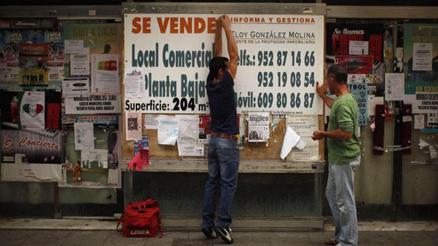 Dos trabajadores cuelgan un cartel que anuncia la venta de locales comerciales en Ronda.