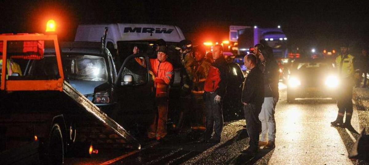 Guardias civiles, conductores y bomberos, junto a algunos de los vehículos implicados. Detrás una cola cada vez mayor de conductores retenidos en la A-52. // Brais Lorenzo