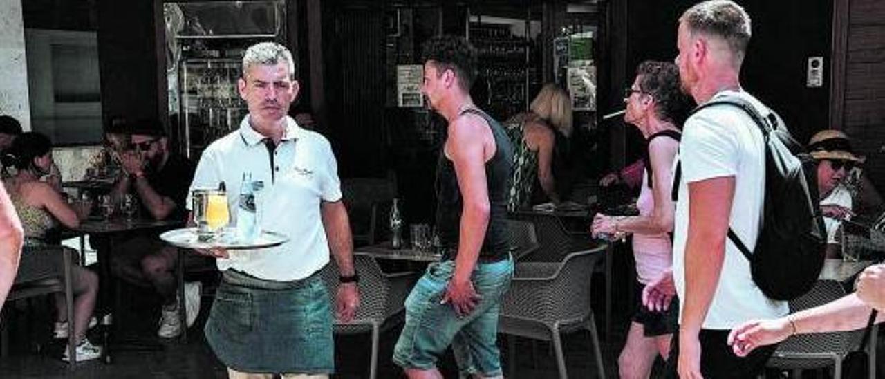 Un trabajador sale de un bar mientras pasean los turistas.  | B.ARZAYUS