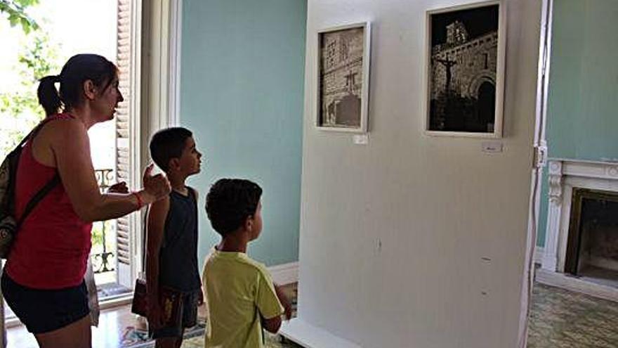 Una madres y dos hijos observan dos fotografías de la exposición.