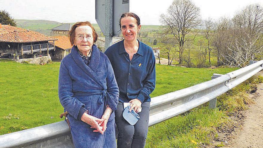 Paz González y Engracia García, sentadas en un quitamiedos de una carretera secundaria que accede a la AS-216. | D. Á.