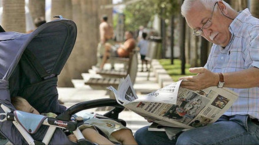 Un abuelo lee el periódico junto a su nieto, en sillita.