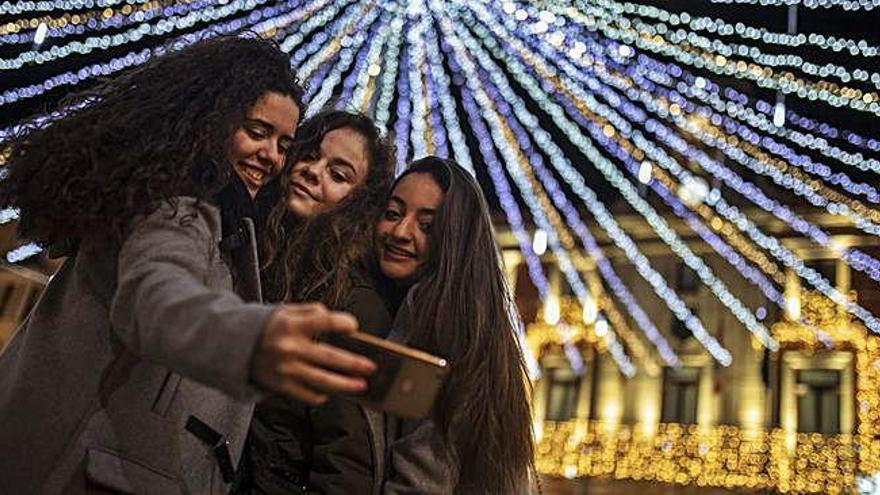 Tres jóvenes se hacen un selfie en la Plaza Mayor de Zamora con la iluminación navideña de fondo.