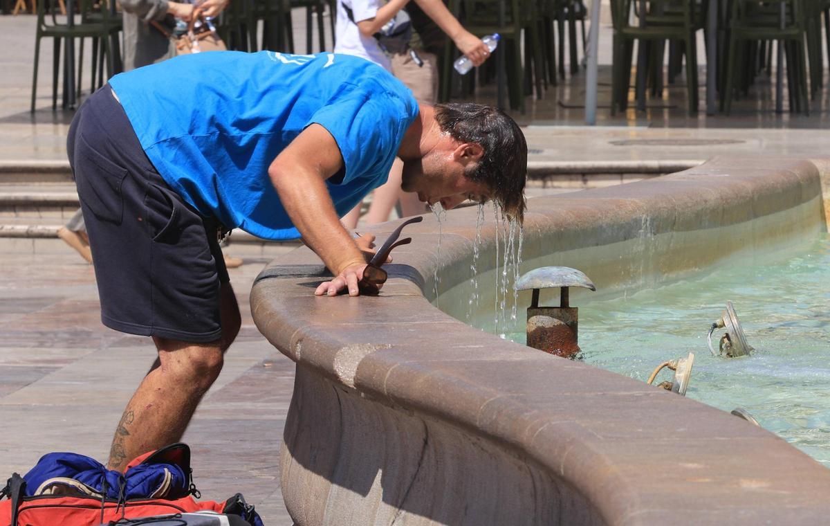 Un hombre se moja la cabeza para combatir el calor en la fuente de la plaza de la Virgen de València.