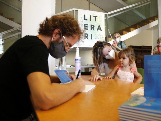 L'autor Jordi Villacampa signant un exemplar del seu nou llibre, 'La ciutat dels nens i les nenes Llunicity', a una nena i a la seva mare en motiu del Sant Jordi d'estiu.
