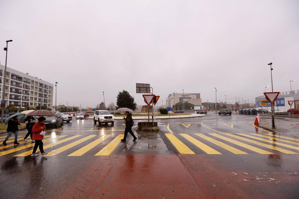 Gente con paraguas cruza por uno de los pasos de peatones de la rotonda del Hipercor.