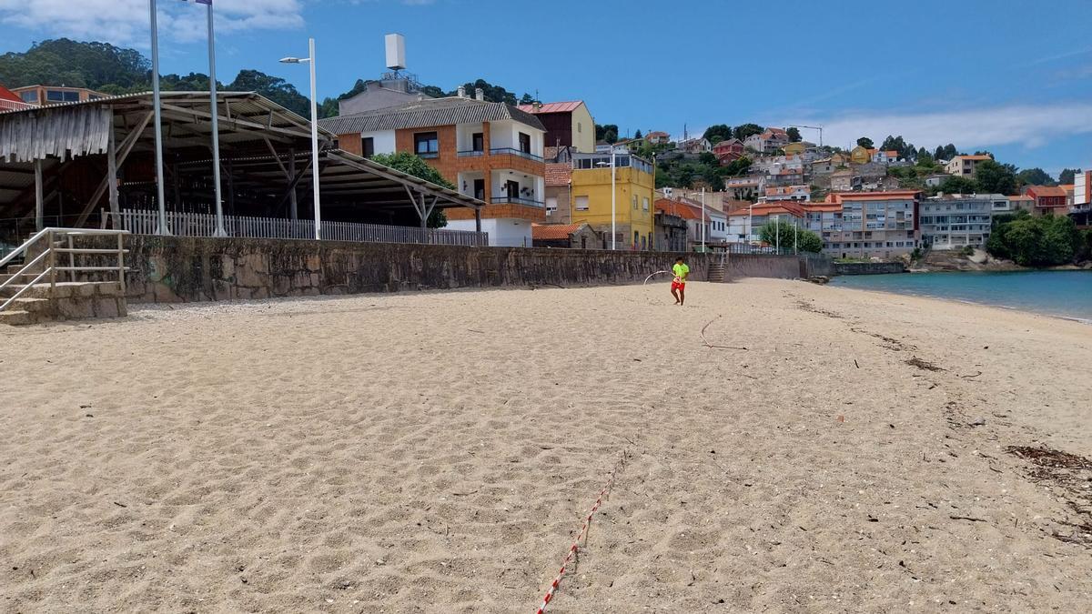 La playa de Banda do Río con la bandera roja este verano y con uno de los socorristas retirando el precinto al final del primer episodio de contaminación registrado en agosto.