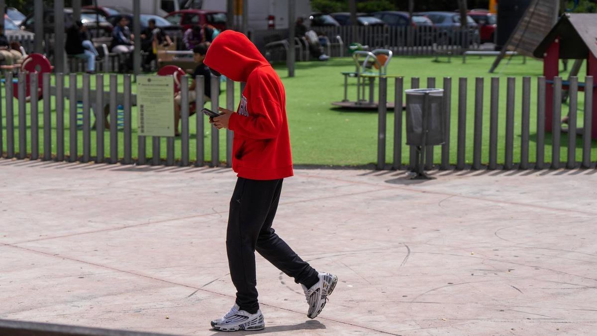 Un menor consulta su teléfono mientras pasa por un parque, esta semana en Barcelona.
