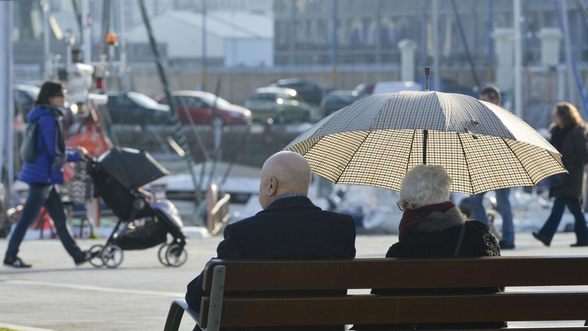 Dos personas, una con paraguas, al sol en la Marina coruñesa un día de primavera.