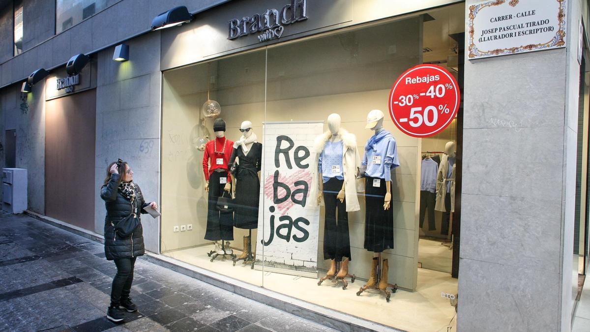 Una mujer contempla un escaparate con carteles de la campaña de Rebajas en el centro de Castelló este domingo.