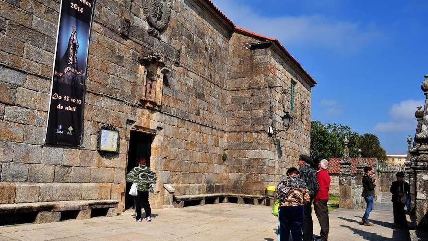 Unos turistas junto a la iglesia de Fefiñáns, de la que cuelga una banderola de la Semana Santa. // I.Abella