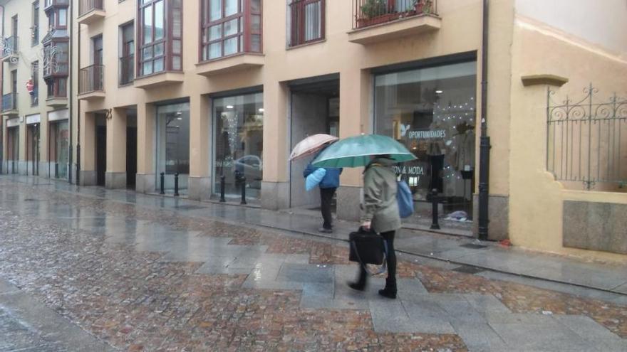 Varios transeúntes se protegen de la lluvia con paraguas esta mañana