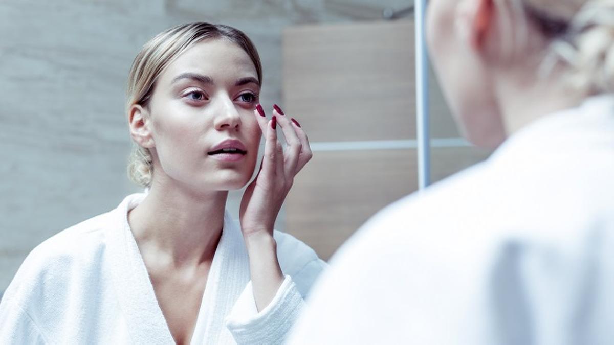 Mujer, aplicándose una mascarilla frente al espejo