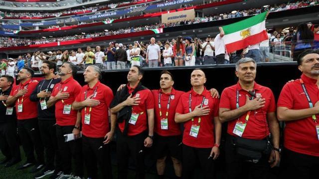 El cos tècnic de l’Iran escolta l’himne amb una bandera persa darrere. | HARRY HOW / AFP
