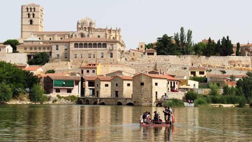 La barcaza surca el río Duero con el esplendor del románico de fondo.