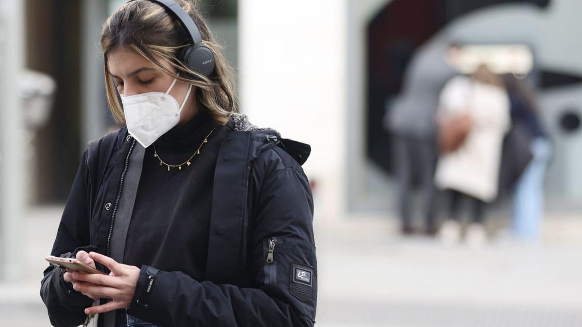 Una jove amb mascareta consulta el seu mòbil al mig del carrer