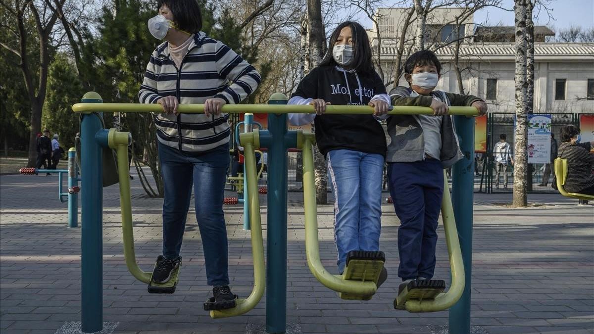 Una familia china se protege con máscaras mientras hace ejercicio en un parque de Pekín, este domingo.