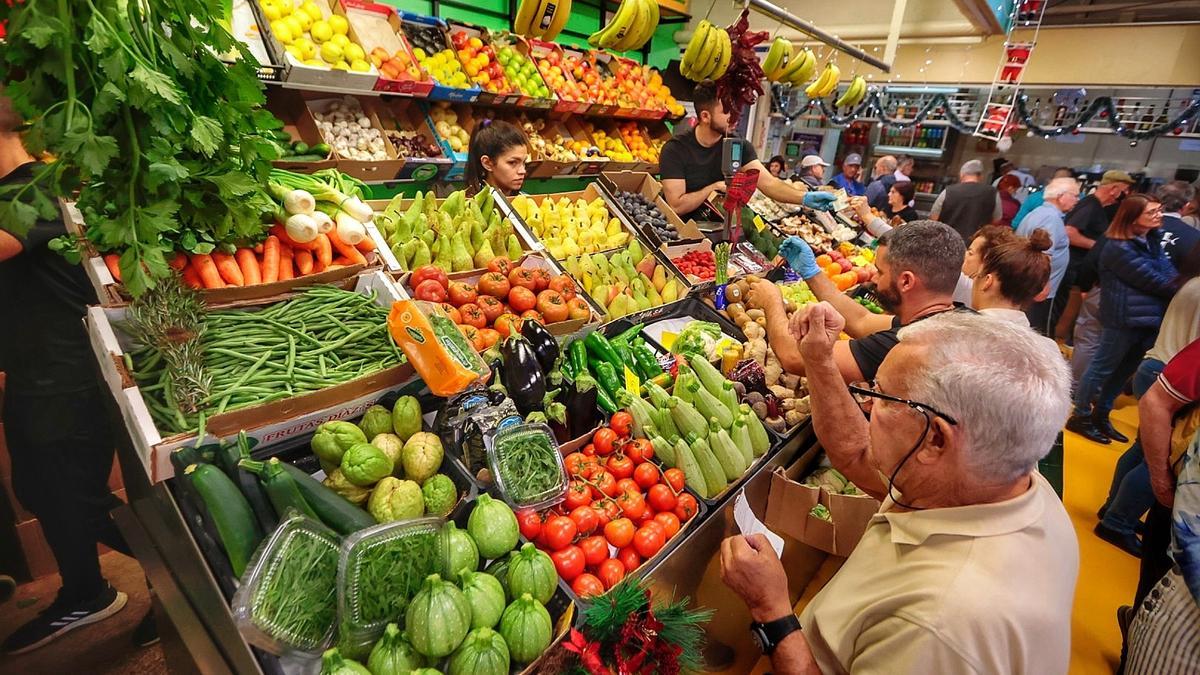 Varios clientes en un puesto de frutas y verduras de un mercado.