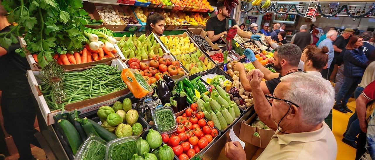 Varios clientes en un puesto de frutas y verduras de un mercado.