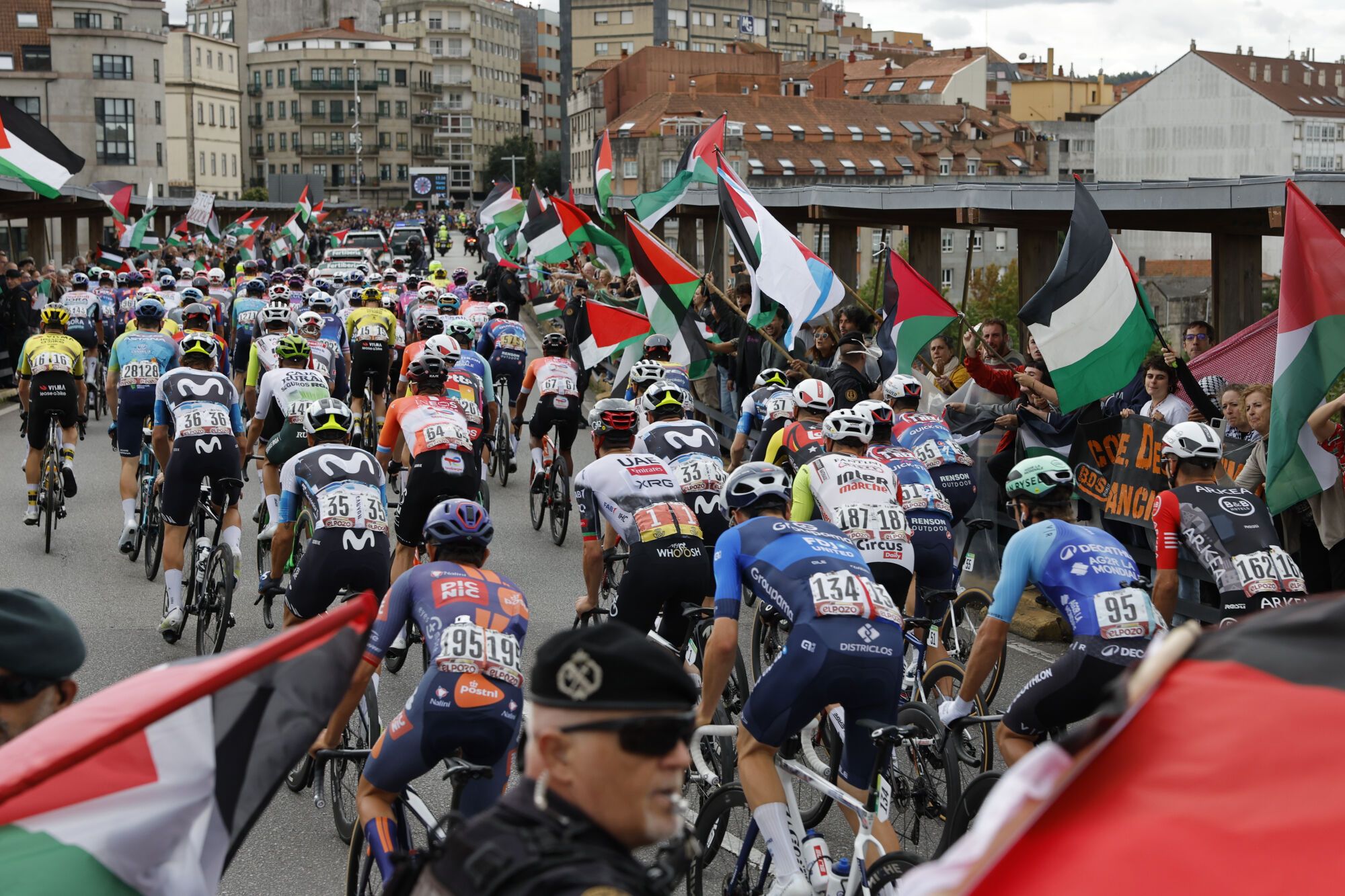 POIO (PONTEVEDRA), 09/09/2025.-El pelotón pasa ante la protetas propalestina durante la etapa 16 de la Vuelta Ciclista a España que se disputa este martes entre Poio y Mos-Castro de Herville (Pontevedra), de 167.9 km de recorrido. EFE/Lavandeira