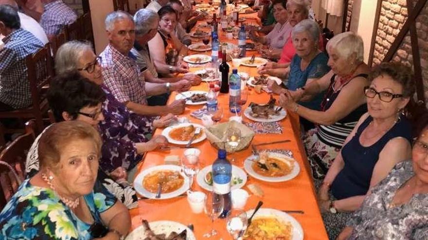 Algunos participantes en la comida vecinal celebrada en Muelas que reunió a numerosas personas. A la derecha, preparativos de la parrillada.