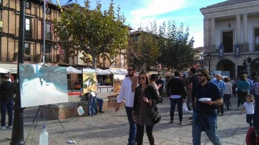 Viandantes contemplan las obras expuestas en la Plaza Mayor.