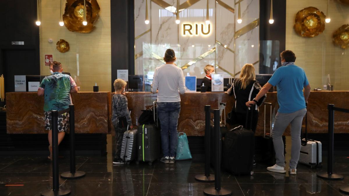 Turistas esperan para ser atendidos en la recepción de un hotel.